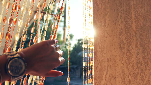 Beaded curtain in the sunlight. Person is parting/moving aside the curtain to see the sunlight