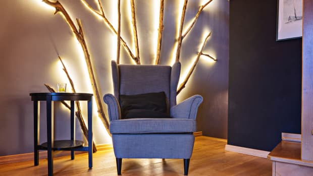 Vintage armchair in living room with homemade tree branch led-lamp on wall, DIY interior detail