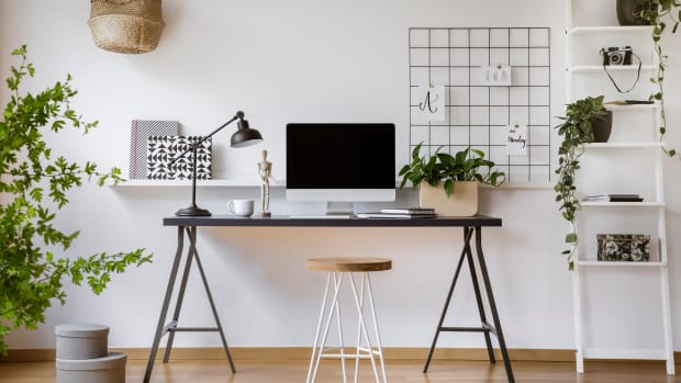 Hairpin stool standing by the wooden desk with mockup computer screen, metal lamp and coffee cup in real photo of white home office interior