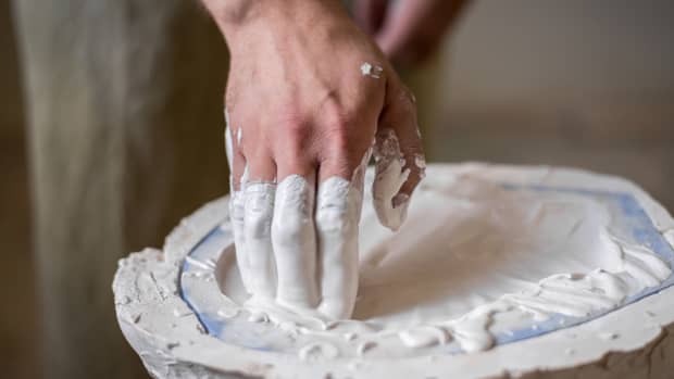 The sculptor's hands fill the white liquid into the mold